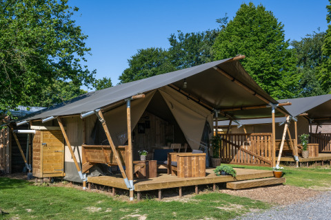 Tienda safari con instalaciones sanitarias, terraza de madera y muebles al aire libre en entorno verde.