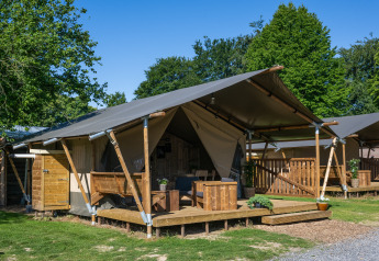 Tienda safari con instalaciones sanitarias, terraza de madera y muebles al aire libre en entorno verde.