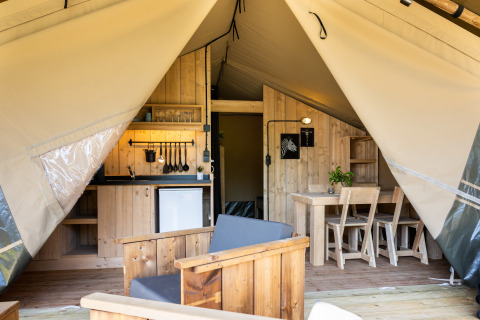 Interior de una tienda safari con cocina, mesa de comedor y asientos en Camping Mareveld, Países Bajos.