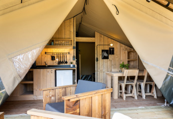 Interior de una tienda safari con cocina, mesa de comedor y asientos en Camping Mareveld, Países Bajos.