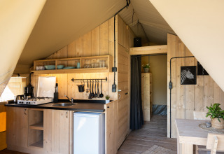 Interieur van een safaritent met houten keuken, eethoek en privé badkamervoorzieningen zichtbaar.