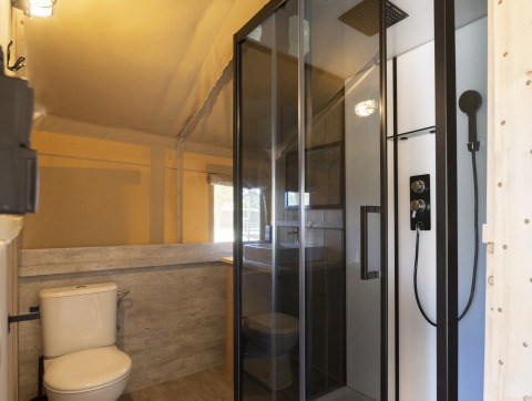 Baño en tienda safari con ducha moderna, inodoro y lavamanos, ideal para una experiencia glamping.