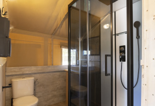 Baño en tienda safari con ducha moderna, inodoro y lavamanos, ideal para una experiencia glamping.