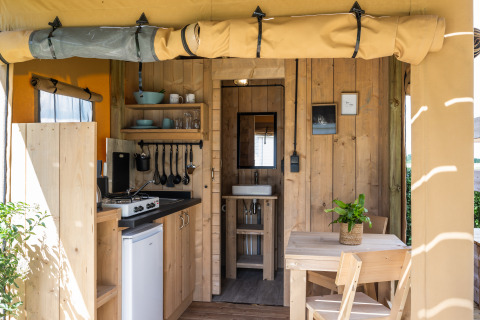 Interior de tienda safari de lujo con cocina, mesa de comedor y baño en Camping Mareveld, Países Bajos.