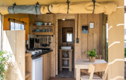 Interiør af en luksuriøs safariteltsuite med køkken, spisebord og badeværelse på Camping Mareveld.