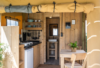 Interior de tienda safari de lujo con cocina, mesa de comedor y baño en Camping Mareveld, Países Bajos.