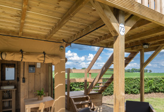 Safaritent met sanitair bij Camping Mareveld, houten terras en trap, groene velden in Nederland zichtbaar.