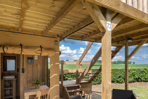 Tienda safari con instalaciones sanitarias en Camping Mareveld, terraza de madera, campos en los Países Bajos.