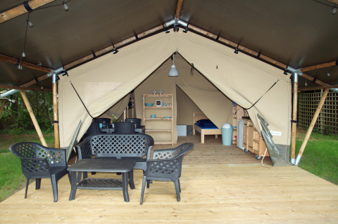 Safari tent with wooden deck, black patio furniture, and visible interior including beds and shelving in nature.