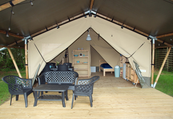 Safari tent with wooden deck, black patio furniture, and visible interior including beds and shelving in nature.
