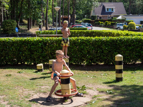 Deux enfants jouent sous le soleil sur une aire de jeux entourée de haies à Recreatiepark de Wrange, Gelderland.