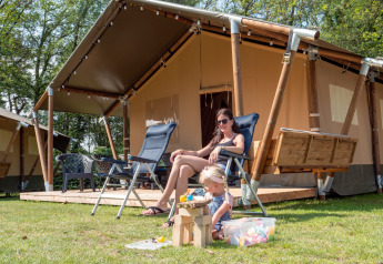 Mutter und Kind entspannen vor einem luxuriösen Safarizelt mit Sanitäranlage im Recreatiepark de Wrange.