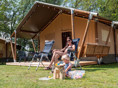 Mutter und Kind entspannen vor einem luxuriösen Safarizelt mit Sanitäranlage im Recreatiepark de Wrange.
