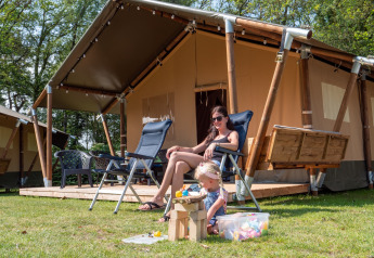 Mutter und Kind entspannen vor einem luxuriösen Safarizelt mit Sanitäranlage im Recreatiepark de Wrange.