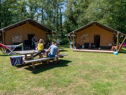 Familias disfrutando de tiendas safari con baño privado en Recreatiepark de Wrange, Países Bajos, rodeados de naturaleza.