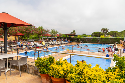 Zona de piscina con personas y tumbonas en Camping del Mar, un parque vacacional en Cataluña, España.