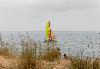 Catamarano dai colori vivaci naviga vicino alle dune erbose al Camping del Mar, Catalogna, Spagna.