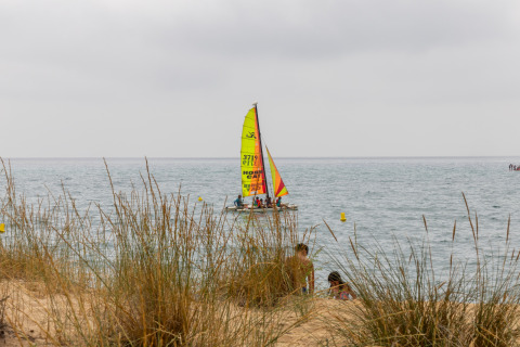Catamarano dai colori vivaci naviga vicino alle dune erbose al Camping del Mar, Catalogna, Spagna.