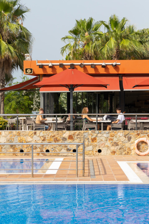 Restaurante al aire libre en Camping del Mar, Cataluña, España, con personas comiendo y piscina a la vista.