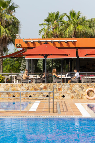 Restaurant en plein air au Camping del Mar, Catalogne, Espagne, avec clients et vue sur la piscine.