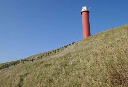 Faro rojo sobre una colina cubierta de pasto bajo un cielo azul claro cerca de Oudesluis, en Holanda Septentrional.