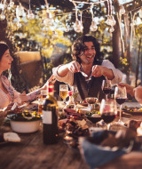 Des amis partagent un repas en plein air sous des guirlandes lumineuses dans un parc avec hébergements glamping.