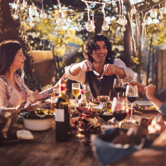Amigos disfrutan de una comida al aire libre bajo luces en un parque vacacional con alojamiento glamping.