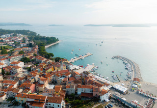 Luftfoto af en kystby i Istrien, Kroatien, med røde tage, lystbådehavn og roligt, blåt havvand.