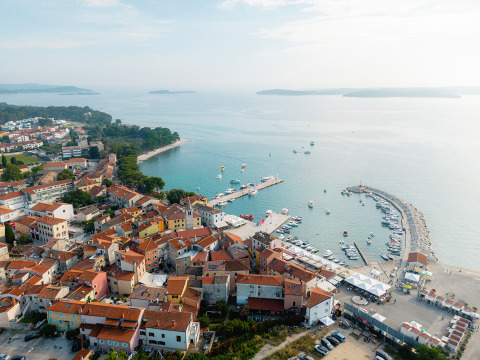Vista aérea de una ciudad costera en Istria, Croacia, con tejados rojos, puerto deportivo y mar azul claro.
