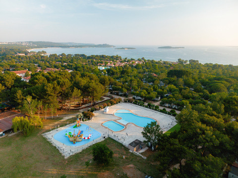 Vista aérea del parque vacacional Bi Village en Istria, Croacia, con piscinas, árboles y el mar al fondo.