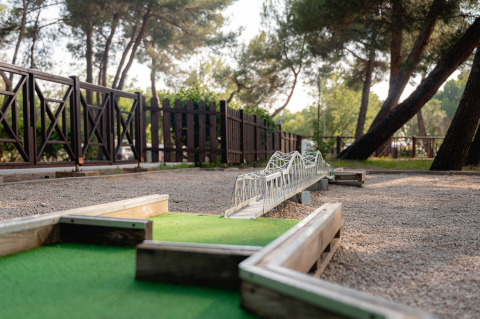Campo de minigolf con obstáculo de puente en un parque vacacional rodeado de árboles en Istria, Croacia.