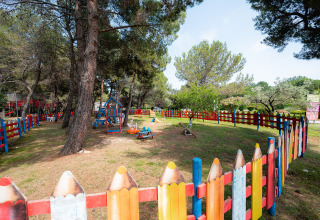 Colorful fenced playground area in a wooded park at Bi Village holiday park, Istria, Croatia, on a sunny day.