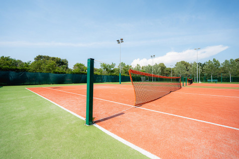 Buiten tennisbaan met rode ondergrond en groene omgeving in Bi Village vakantiepark, Istrië, Kroatië.