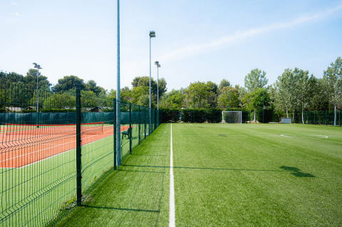 Voetbal- en tennisvelden gescheiden door een hek bij Bi Village vakantiedorp, Istrië, Kroatië, met bomen.