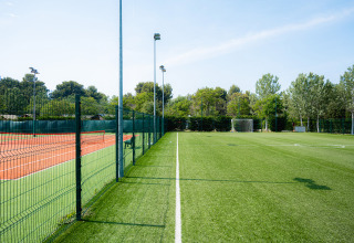 Fodboldbane og tennisbane adskilt af hegn i Bi Village feriepark, Istrien, Kroatien, omgivet af træer.