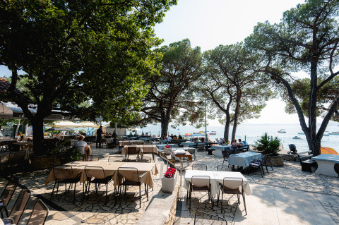 Zona de comedor al aire libre en Bi Village, Istria, Croacia, con mesas bajo árboles y vista al mar.