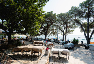 Buitenrestaurant aan het water in Bi Village vakantiepark, Istrië, Kroatië, met schaduwrijke bomen.