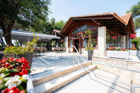 Zona de comedor al aire libre en un restaurante de Bi Village, parque vacacional en Istria, Croacia, rodeado de árboles.