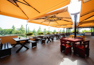 Terraza exterior con sombrillas grandes y mesas de madera en el parque vacacional Bi Village en Istria, Croacia.