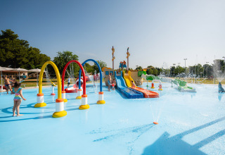 Kinder spielen im bunten Wasserspielplatz mit Rutschen und Fontänen im Bi Village Ferienpark, Istrien, Kroatien.