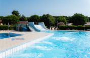 Udendørs swimmingpool med vandrutsjebane på Bi Village feriepark i Istrien, Kroatien, omgivet af grønne træer.
