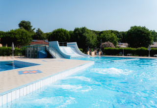 Außenpool mit Wasserrutsche im Bi Village Ferienpark in Istrien, Kroatien, umgeben von Bäumen und Sonnenschirmen.