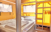 Interior de la tienda safari Villatent Outback con cama y armario en Bi Village, Croacia.
