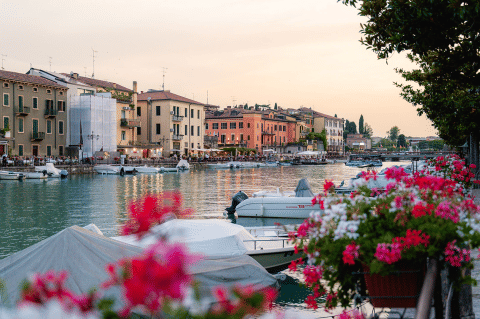 Façade au bord de l’eau au Campeggio del Garda, Vénétie, Italie, avec bateaux, fleurs et bâtiments colorés au crépuscule.