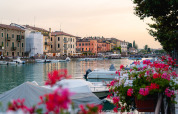 Havnefronten ved Campeggio del Garda i Veneto, Italien, med både, blomster og farverige bygninger ved solnedgang.