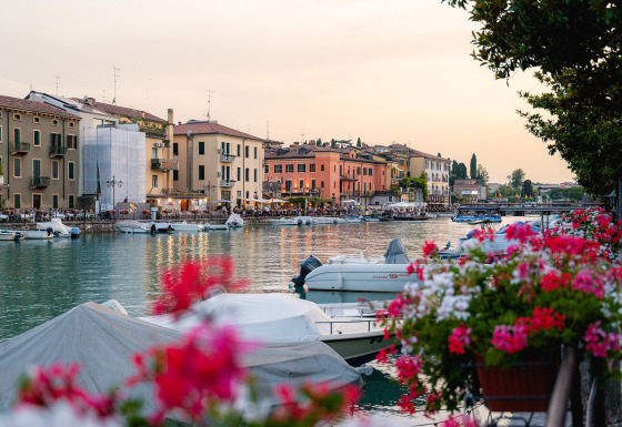 Waterfront at Campeggio del Garda holiday park in Veneto, Italy, with boats, flowers, and colorful buildings at dusk.