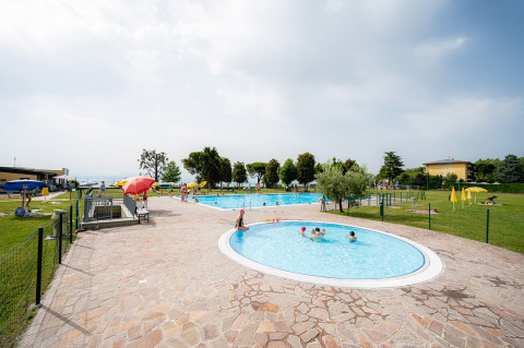 Zona de piscina al aire libre en Campeggio del Garda, un parque vacacional en Veneto, Italia, con niños nadando.