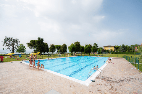 Piscine extérieure avec des personnes, entourée de verdure au Campeggio del Garda, Veneto, Italie.