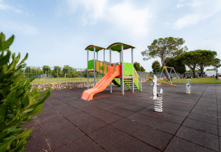 Spielplatz mit Rutsche und Schaukeln im Campeggio del Garda, Veneto, Italien, umgeben von grüner Landschaft.