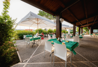 Udendørs spiseområde på Campeggio del Garda med grønne duge, parasoller og moderne stole i Veneto, Italien.